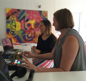 Youth Worker Hayley having a go on a DJ mixer deck, aided by music leader Sophie