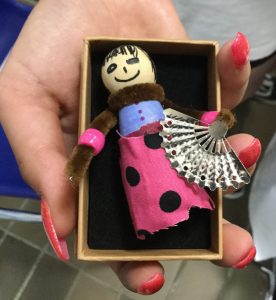A small wooden figure in spotty skirt and with tiny fan, inside a cardboard box