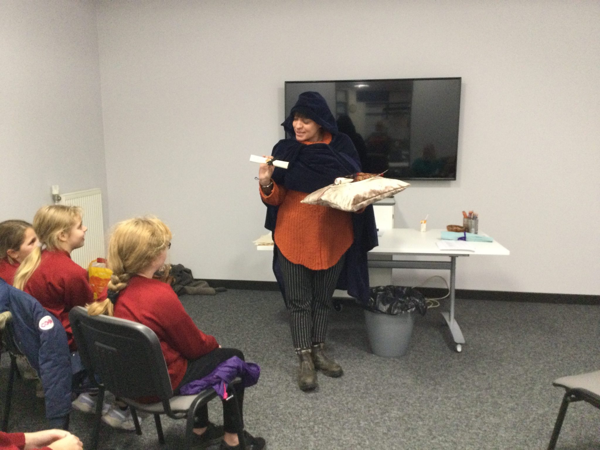 Artist Caitlin dressed in a blue velvet cloak handing out scrolls to the children