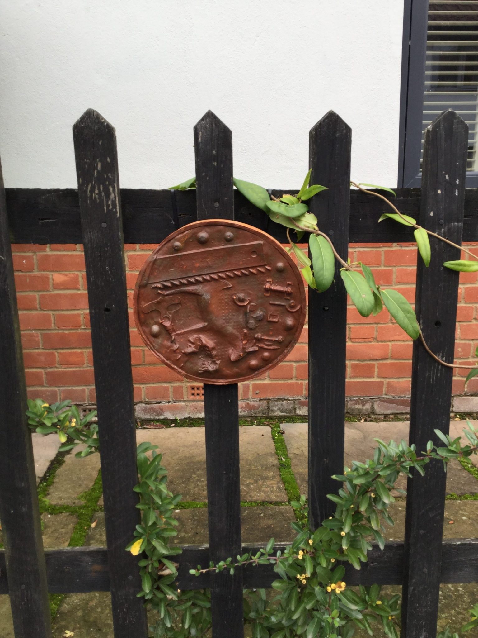 A brown circular plaque with several impressions including an old drill bit, a donkey and marbles