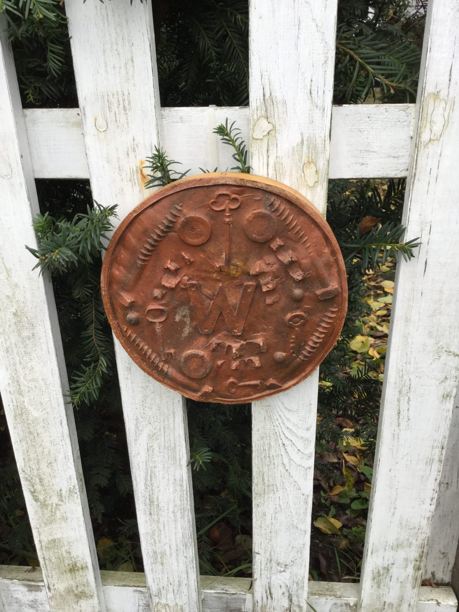 A brown circular plaque with bottle tops, keys and the letter W