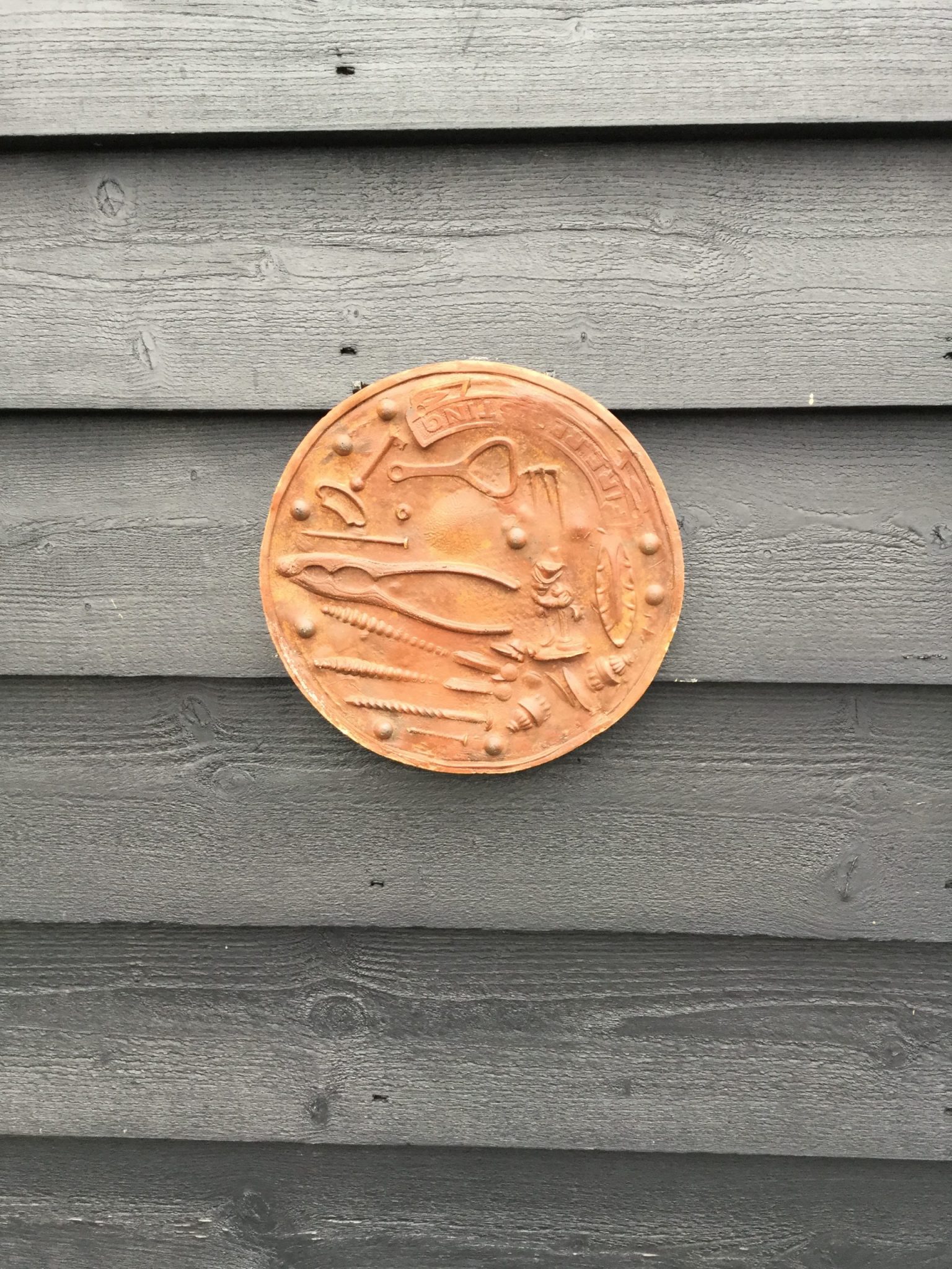 A circular brown plaque, with impressions of bottle openers and nutcrackers