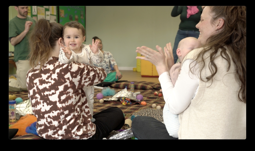 A parent clapping and a child looking at the camera clapping.