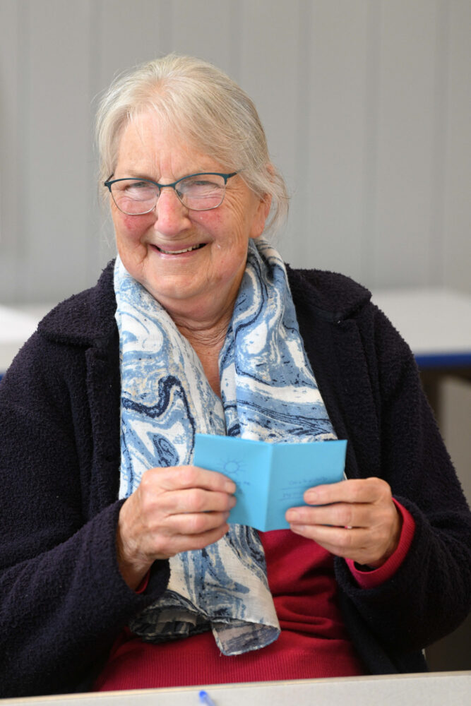 A smiling woman with a handmade card and happy eyes