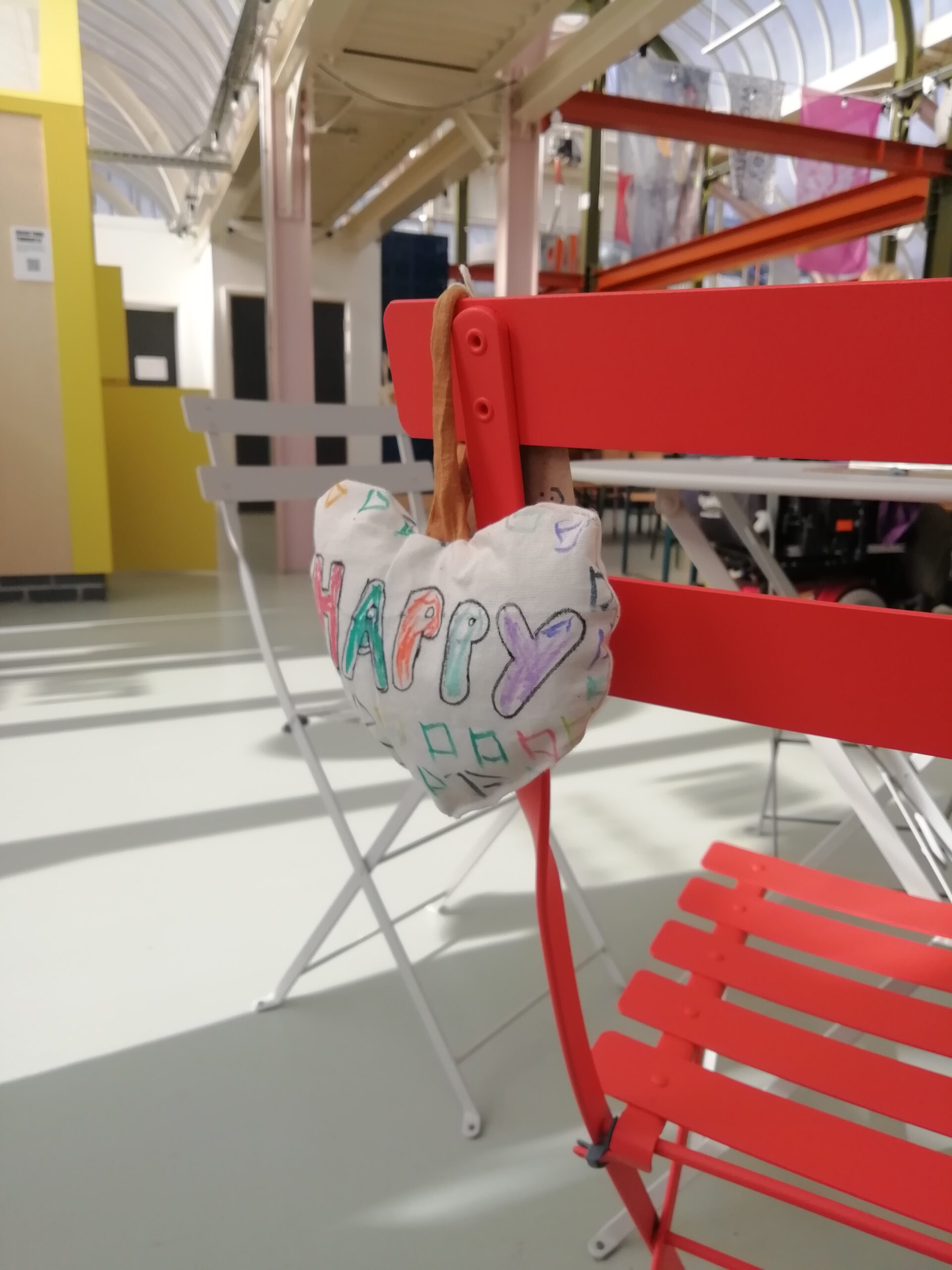 White heart with'happy' written on it in colourful lettering hanging off a red chair