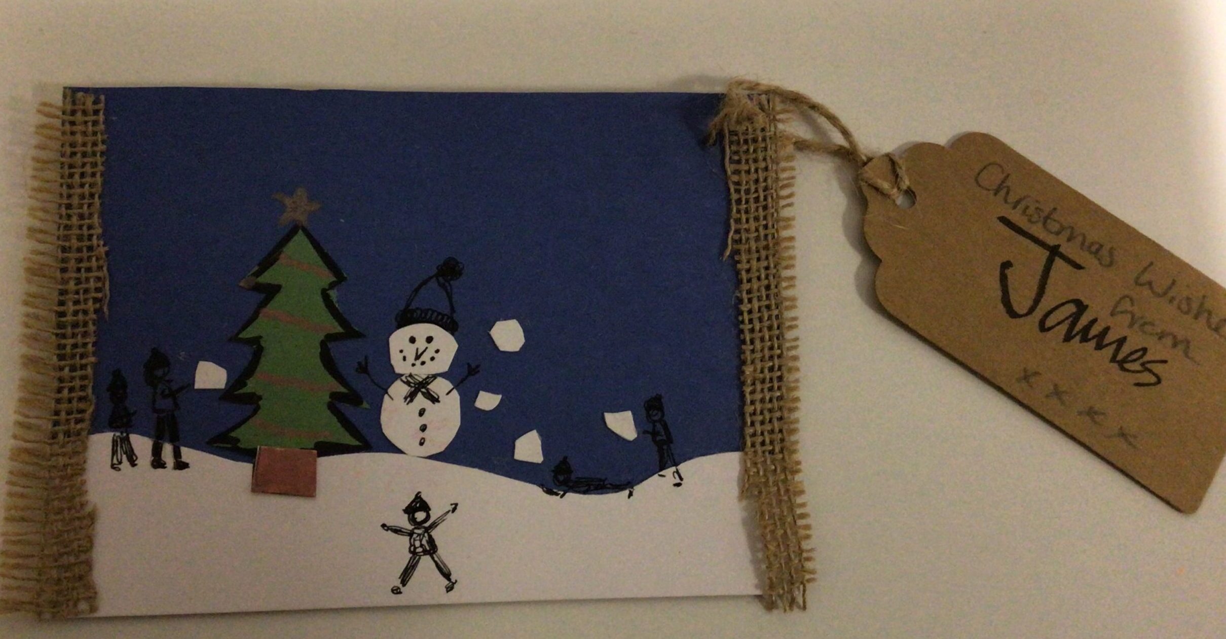 A postcard with a snowman and a Christmas tree with figures playing snowballs.