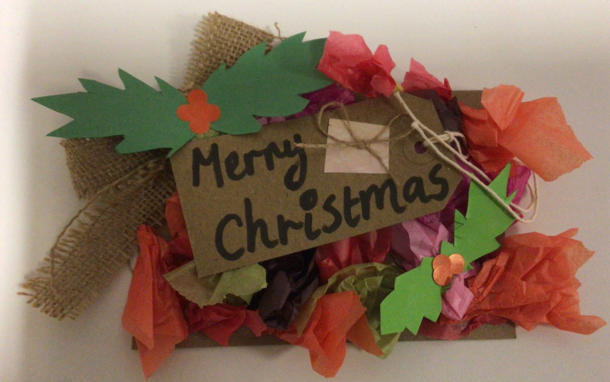A postcard decorated to look like a Christmas wreath with paper holly leaves and tissue paper