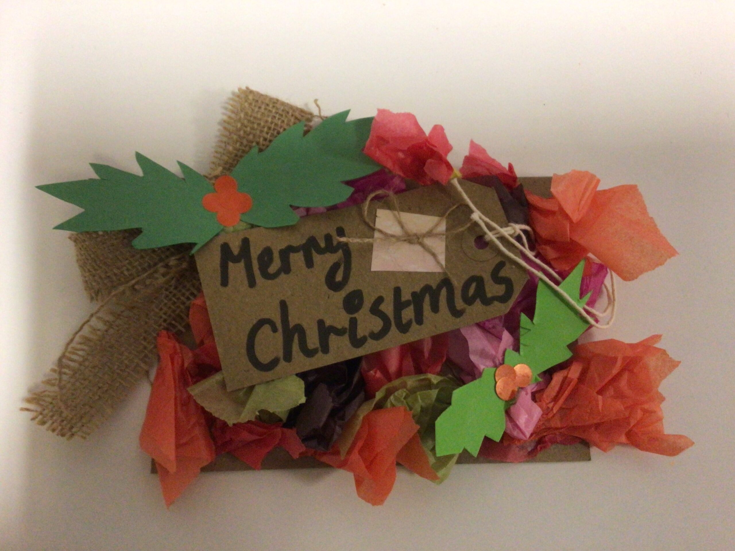 A postcard decorated to look like a Christmas wreath with paper holly leaves and tissue paper