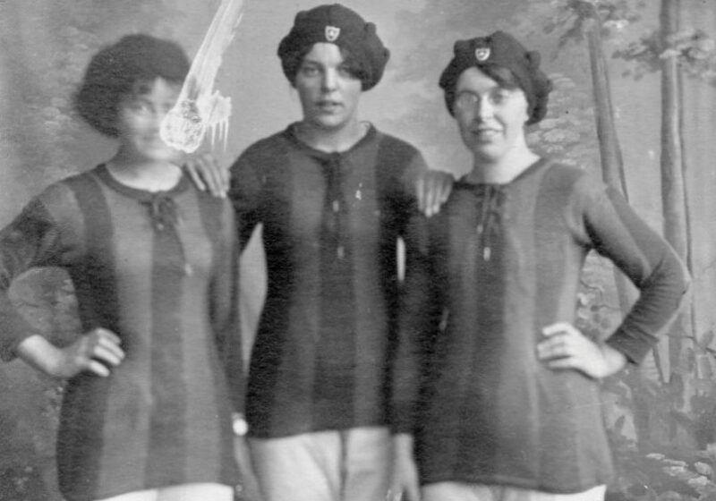 An old monotone photograph of three women stand side by side, they are dressed in vertically striped long sleeved shirts, light coloured shorts and wearing bonnet-like caps on their heads.