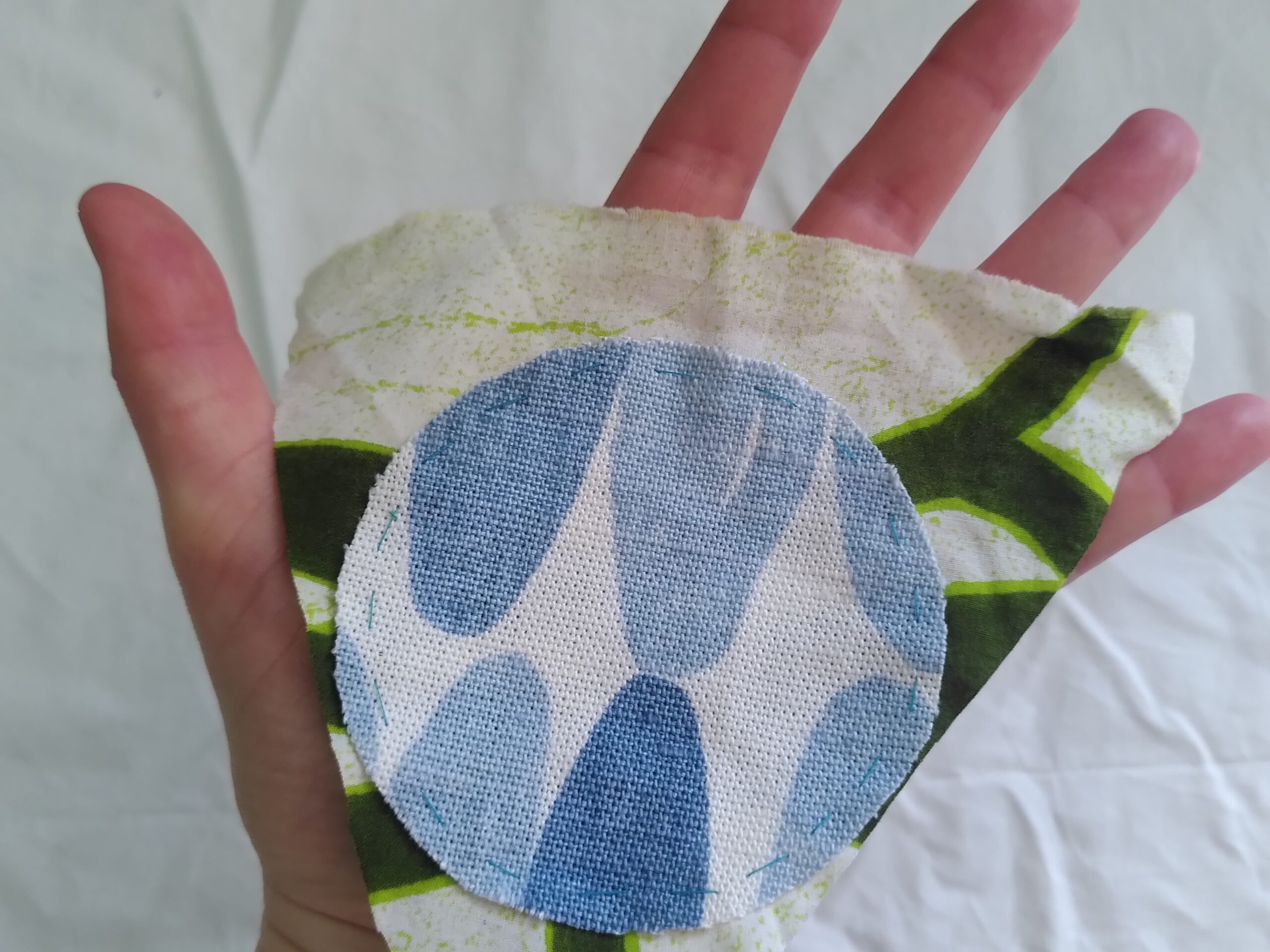 In the palm of a hand is a green and cream coloured bunting flag with a circle of blue and cream fabric placed on top