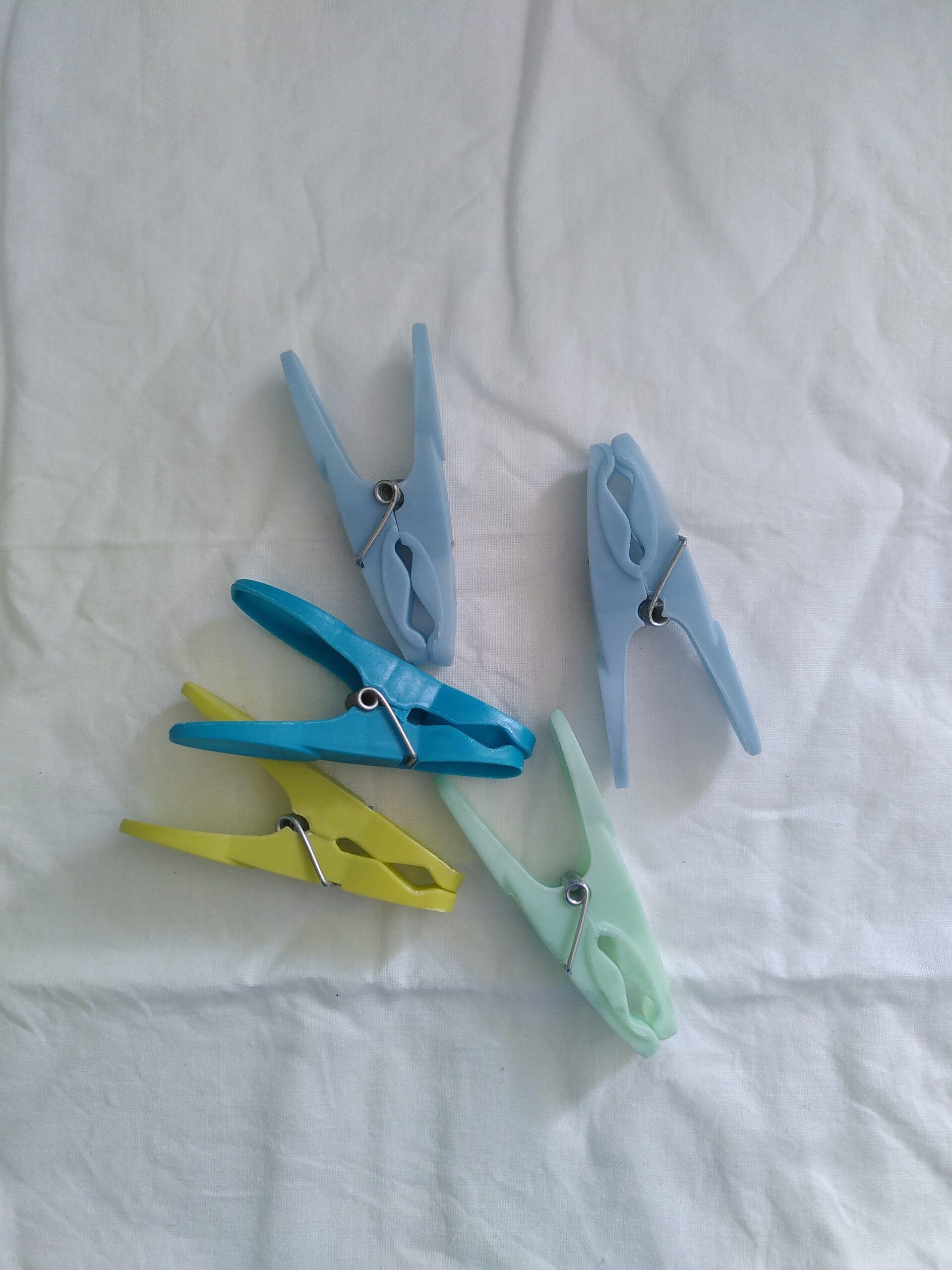 Five plastic pegs, two light blue, one yellow, one light green and the fifth bright blue, lying on a creased white background