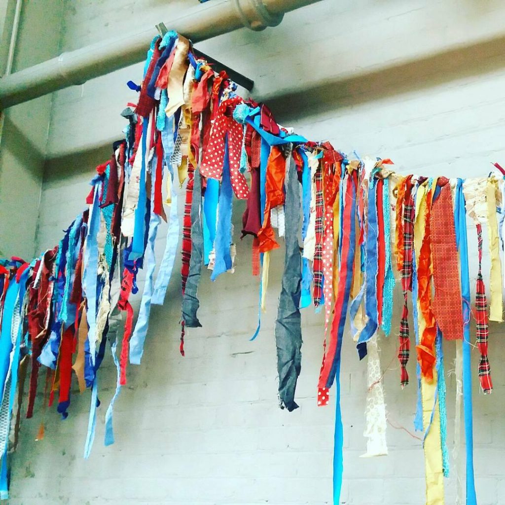 A string of multicoloured rag bunting in which strips of material and ribbons, rather than triangular or square flags have been tied to a length of string to make colourful bunting