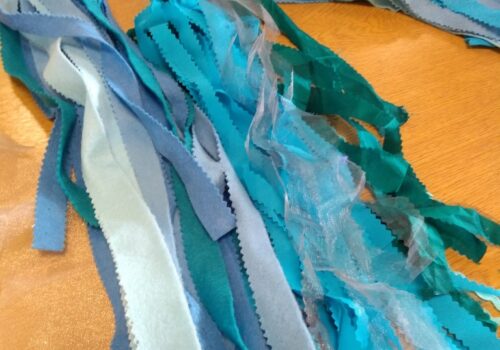 Long strips of blue and green felt and silver netting laid out on a table ready to be made into bunting