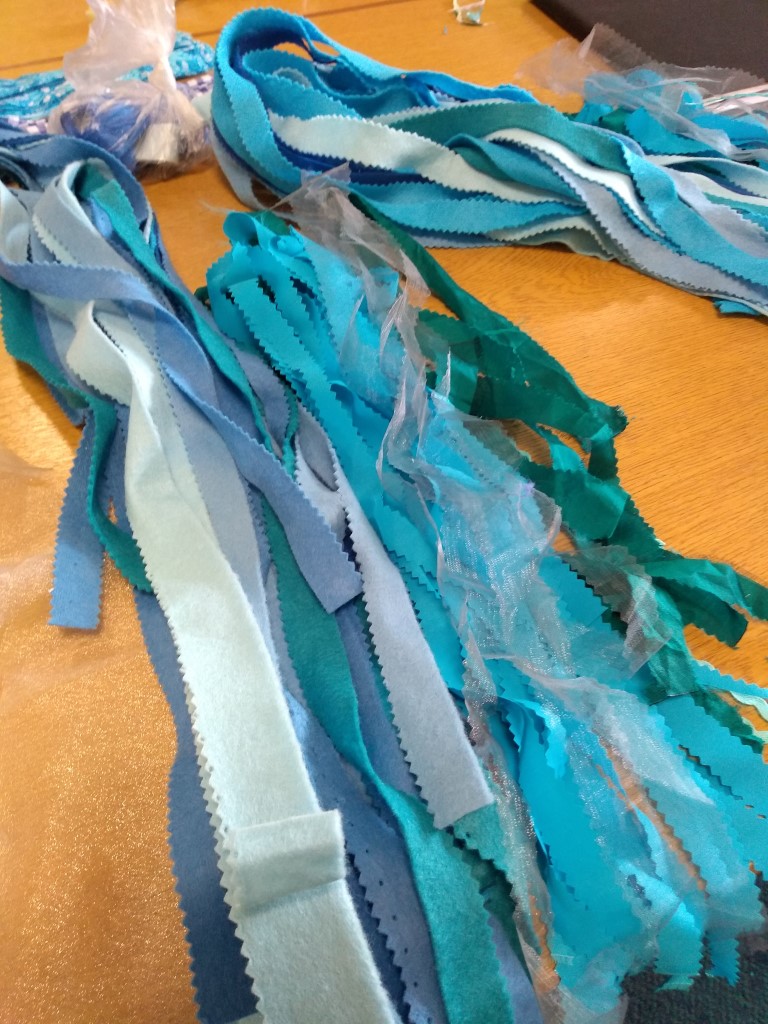 Long strips of blue and green felt and silver netting laid out on a table ready to be made into bunting