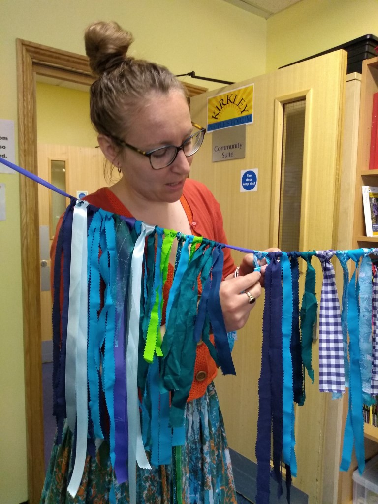 A string of bunting stretches in front of a woman who is tying on more strips of blue fabric