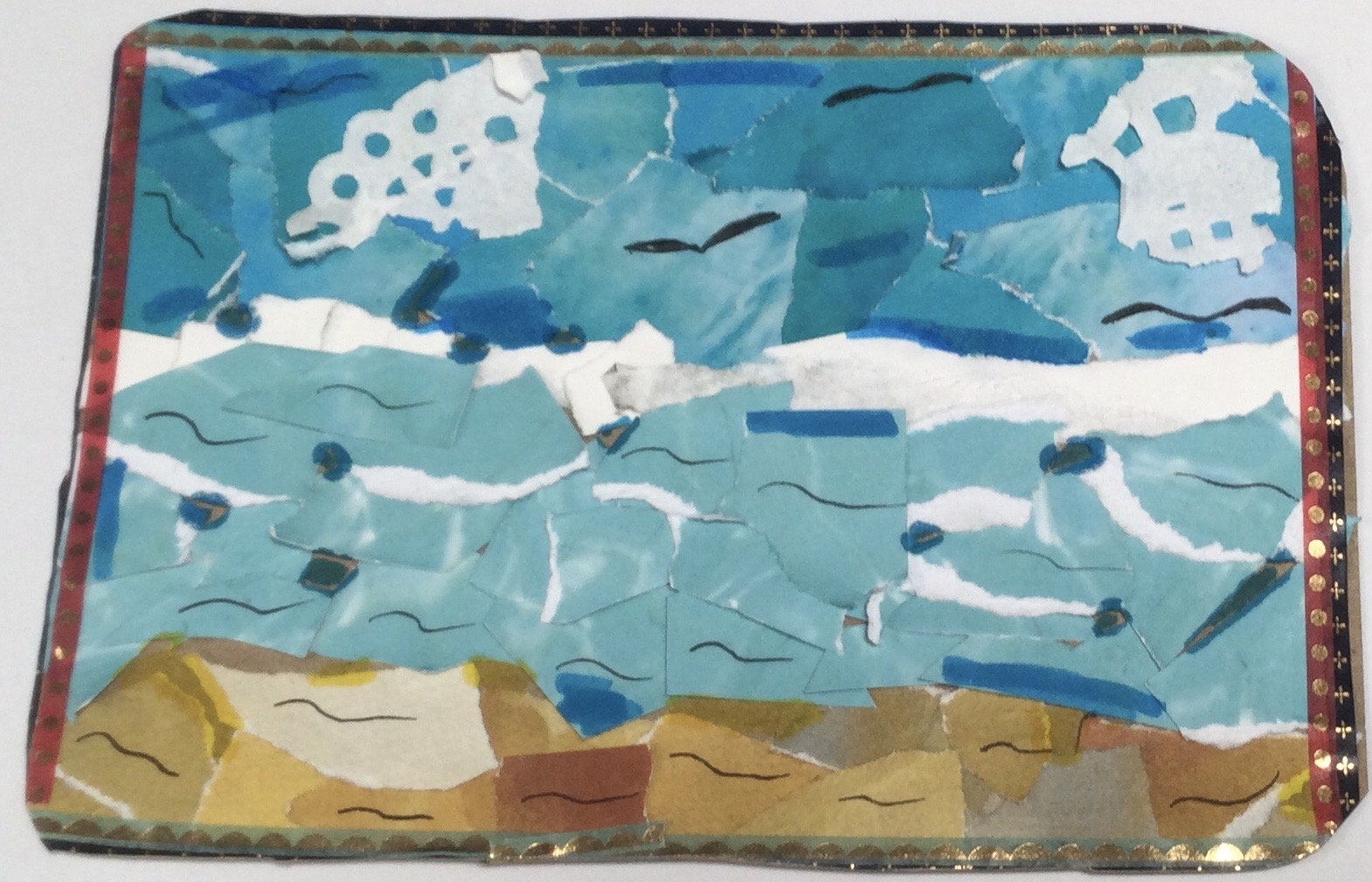 A collaged postcard with an image of sea and sky created with lots of tiny bits of blue paper, details picked out with hand-drawn lines in black and blue. Scraps of yellow and gold paper create a beach effect along the bottom of the card and the whole is bordered in thin tapes of dark blue, red and gold