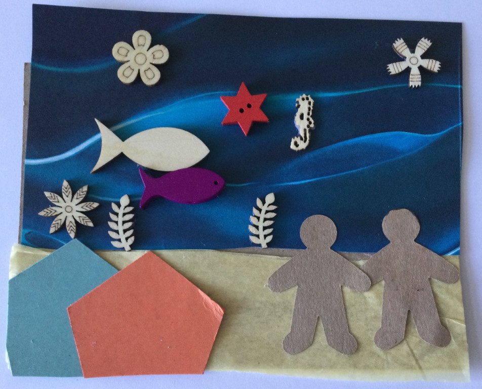 A collaged postcard featuring two brown card figures standing on a yellow tissue paper beach with an orange and a blue paper beach hut in the foreground. A deep blue paper fills the top two thirds of the card and is embellished with wooded shapes including fish, a seahorse, seaweed and stars
