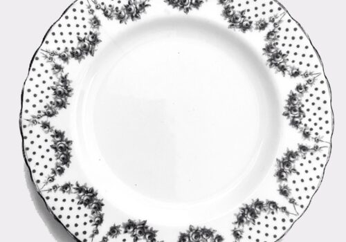 An empty white plate with scalloped edges and an edge decorated with black dots and black and white garlands of roses
