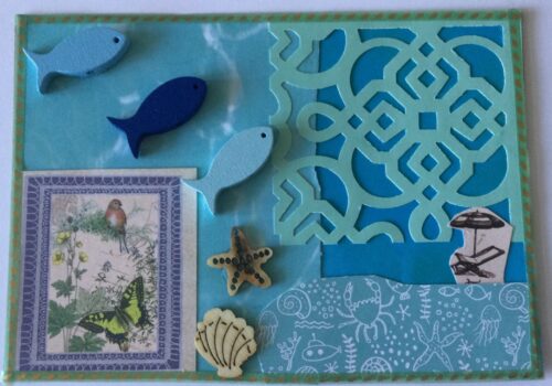 A collaged postcard featuring overlaid pieces of blue patterned papers, including one that is latticed, a tiny picture of a deckchair and beach umbrella, a framed image of a butterfly and a bird and wooden shapes of 3 blue fish, a starfish and a scallop shell