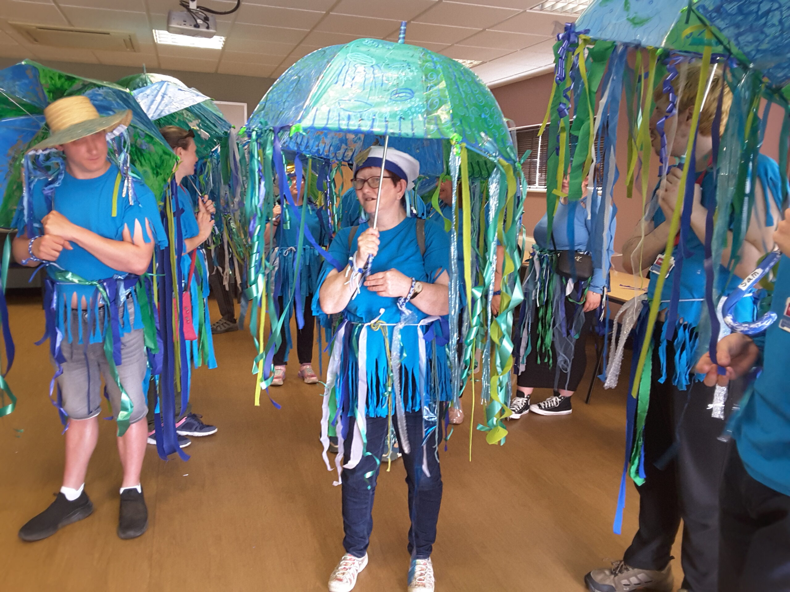 Interior shot of Brave Art participants in fancy dress resembling sea creatures and carrying decorated umbrellas, as they prepare for the big parade