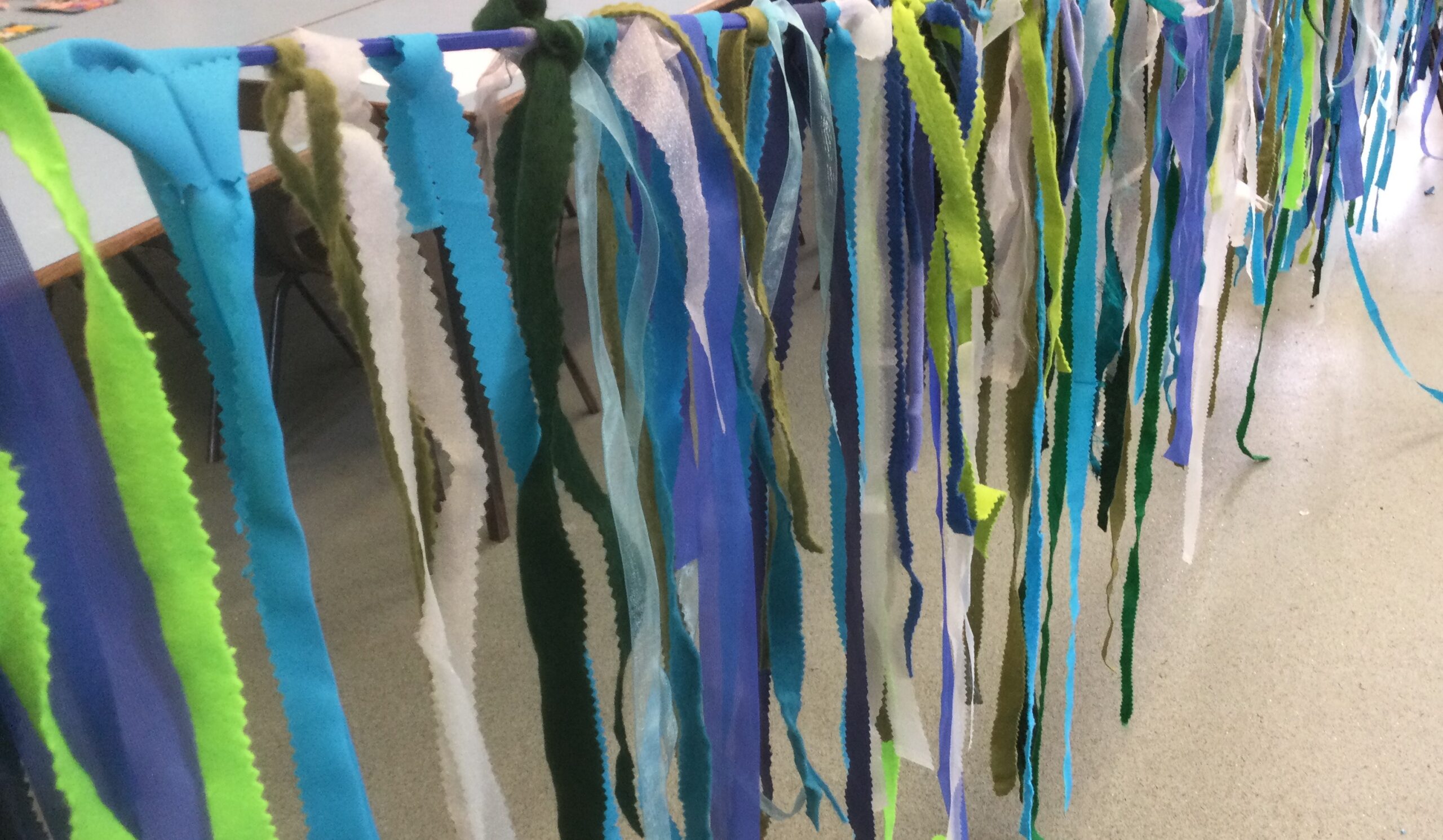 Strips of blue, green and white fabric strung from blue tape to create sea-like bunting