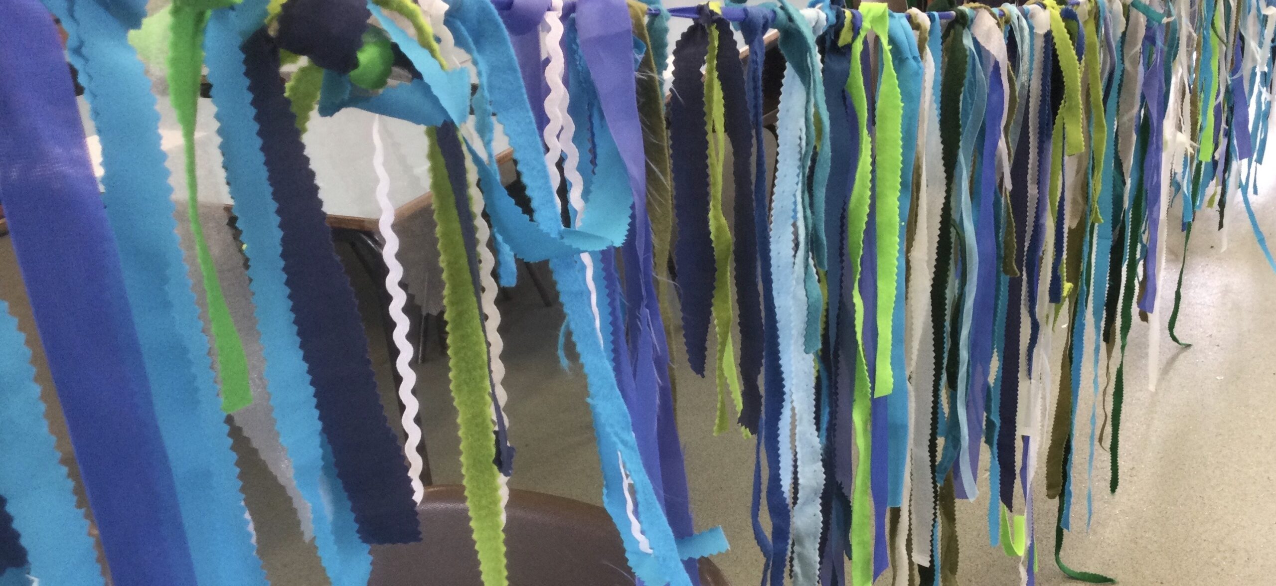Lengths of material in different shades of blue and green, with additions of white ricrac ribbon, tied to a thick blue tape to create sea bunting
