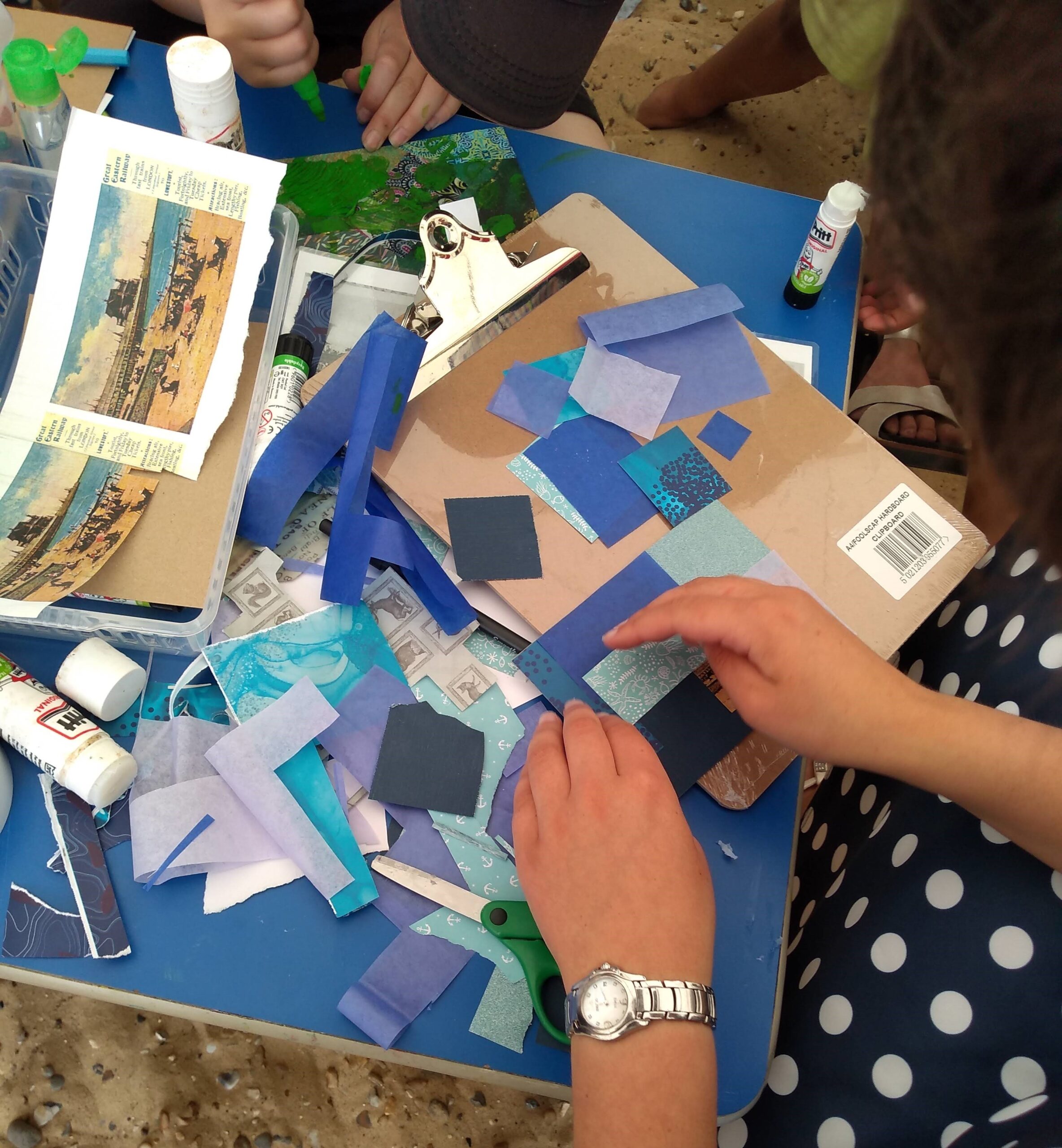 A person wearing a blue and white polka dot dress is seated at a blue-topped table, with piles of assorted papers, all in different shades of blue, in front of them.