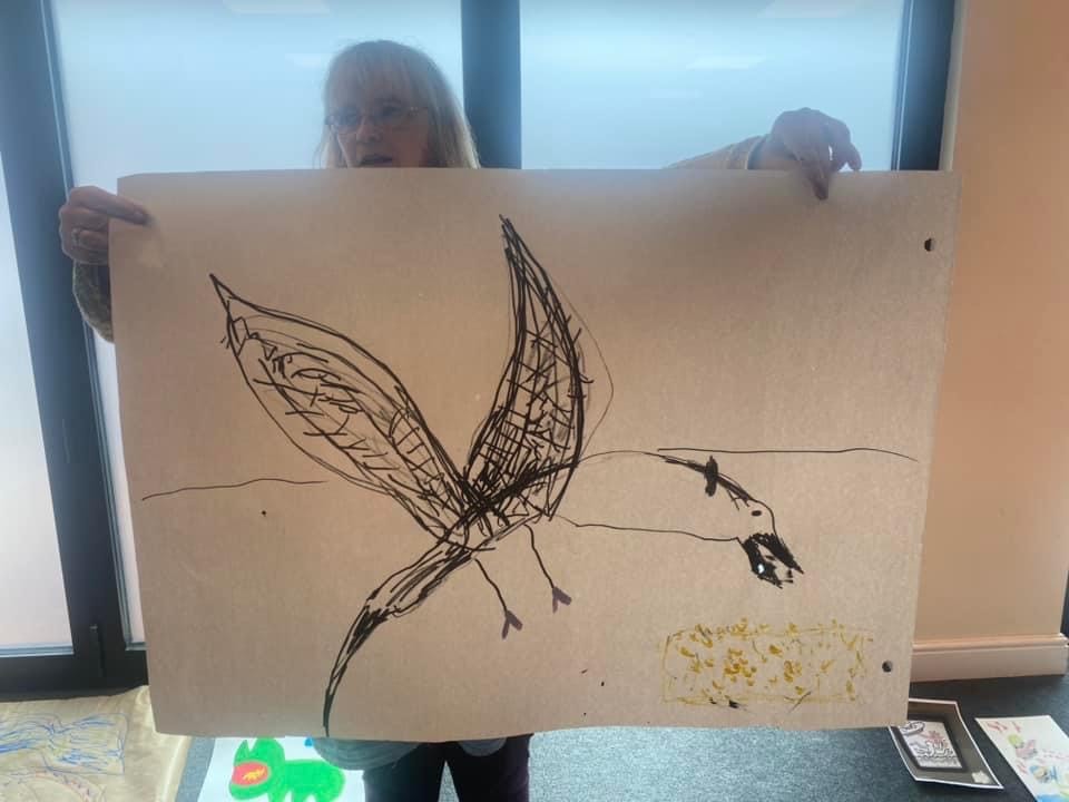 A Brave Artist holding up a large pen and ink drawing of a bird.