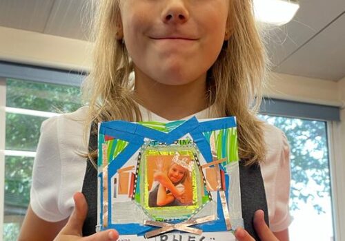 School child holding a decorated card on which she has listed her team skill as Never Being A Sore Loser