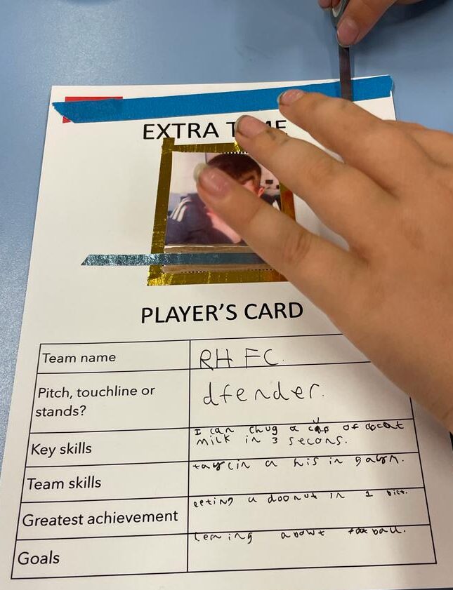 A child's hands, applying decorative tape to a Player's Card on which he has written that his greatest achievement is eating a donut in one bite