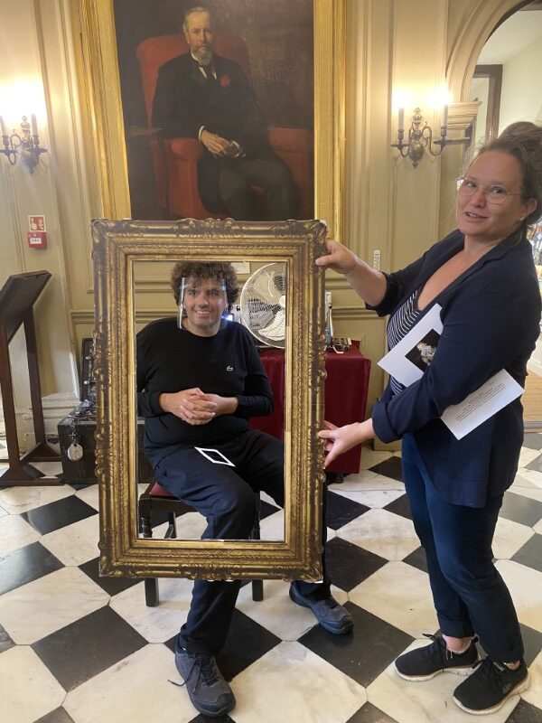 A Brave Art student poses behind a portrait frame