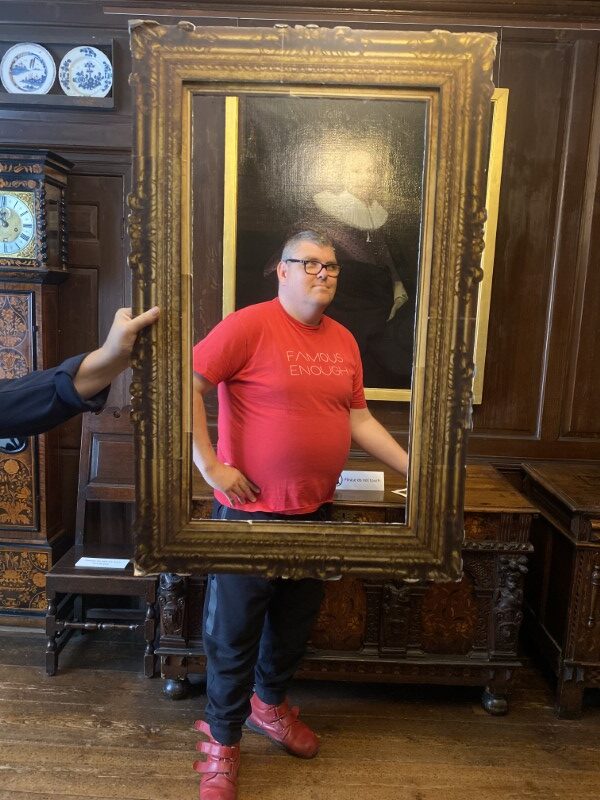 A Brave Art student poses behind a portrait frame