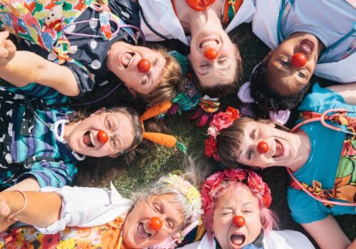 A group photo of seven clowns lying in a circle with heir heads in the centre