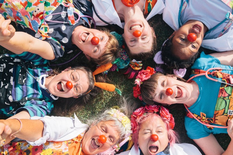 A group photo of seven clowns lying in a circle with heir heads in the centre