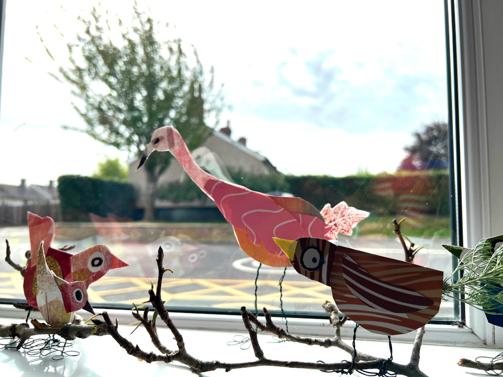 Artworks of colourful birds perched on a branch, displayed in a window.