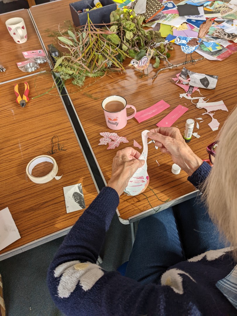 A workshop participant sitting at a table crating three dimensional artworks of colourful birds.