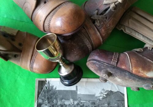 Old brown leather football boots circa 1940's, shin pads, a small silver trophy and a monochrome photograph of a football team