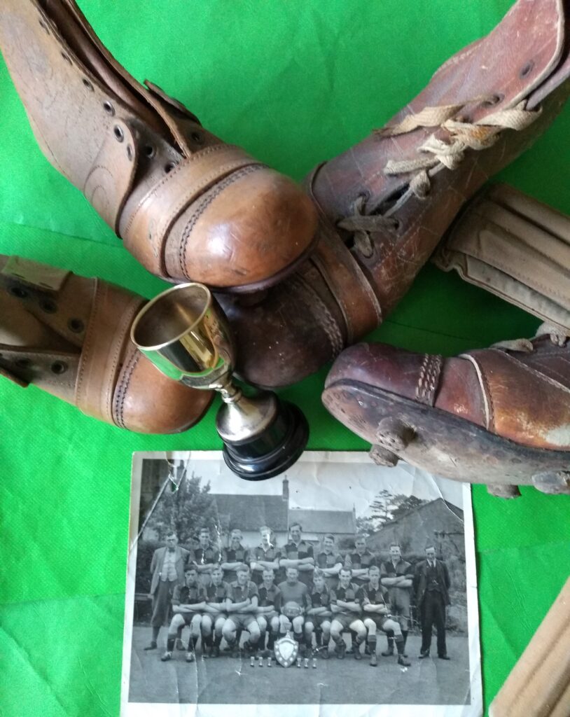 Old brown leather football boots circa 1940's, shin pads, a small silver trophy and a monochrome photograph of a football team