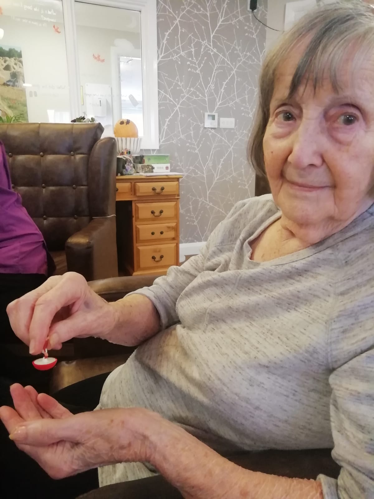 A woman looks into the camera. In her right hand she holds a tiny red and white football figure