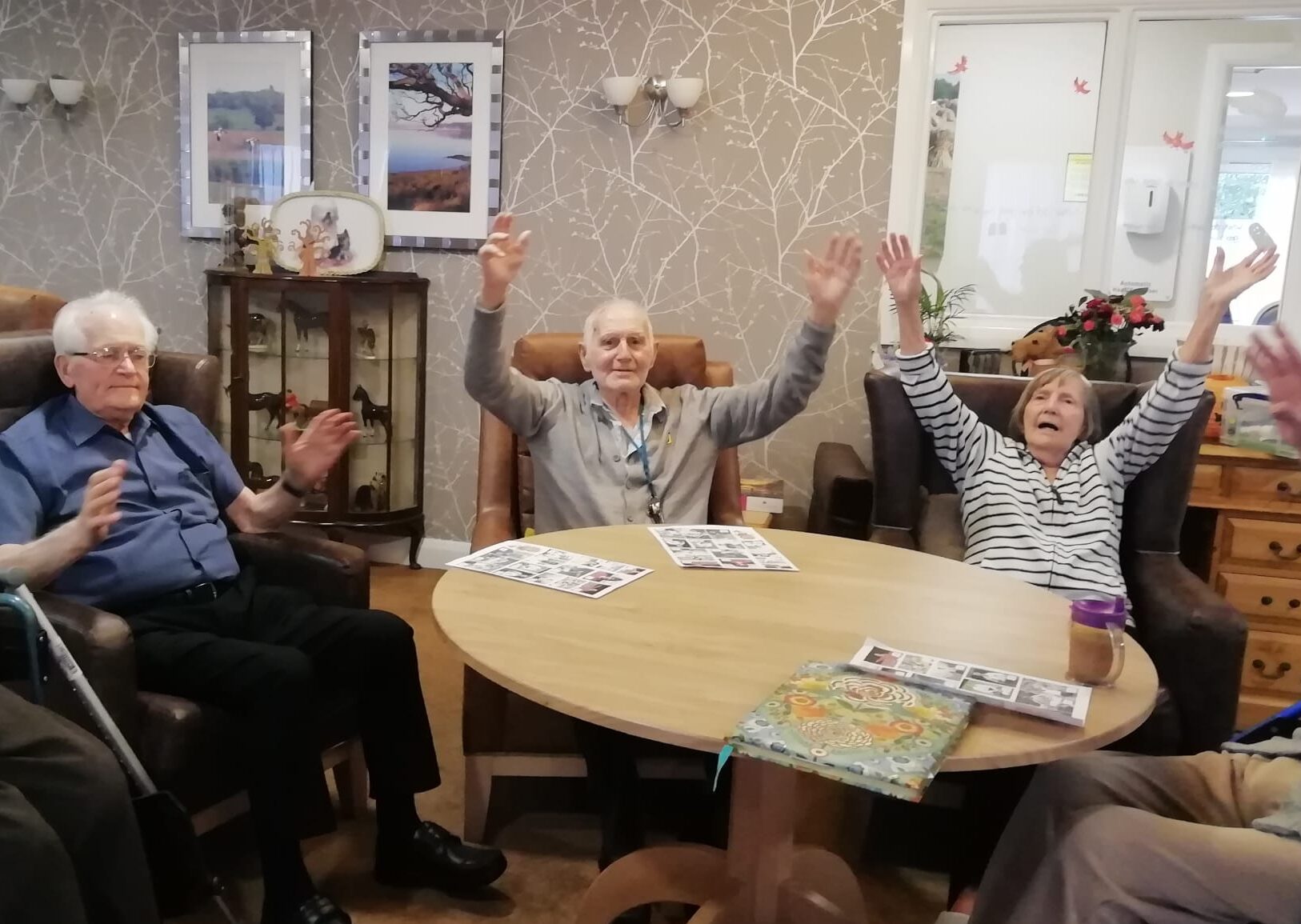 Three adults with their arms in the air and seated around a wooden table