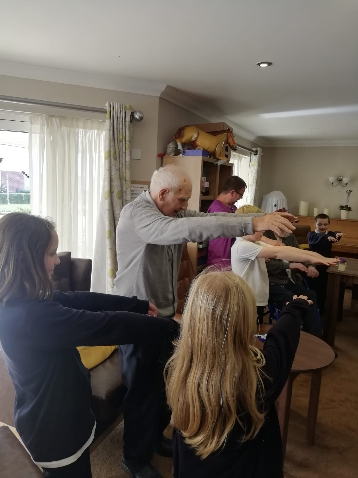 A gentleman stands, arms outstretched with children either side of him, copying his stance