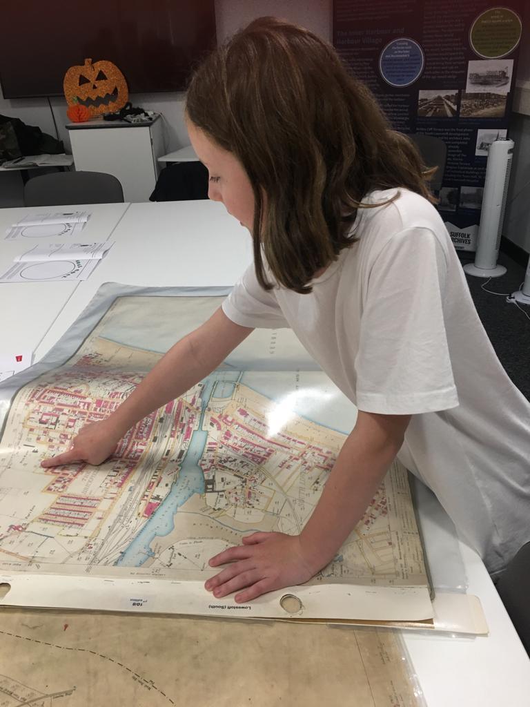 A child with shoulder-length dark hair and wearing a white T-shirt points to an area on an old map