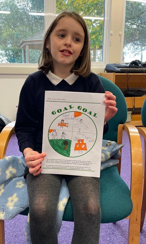 A school girl holds up her worksheet, showing pictures she's drawn in green and orange
