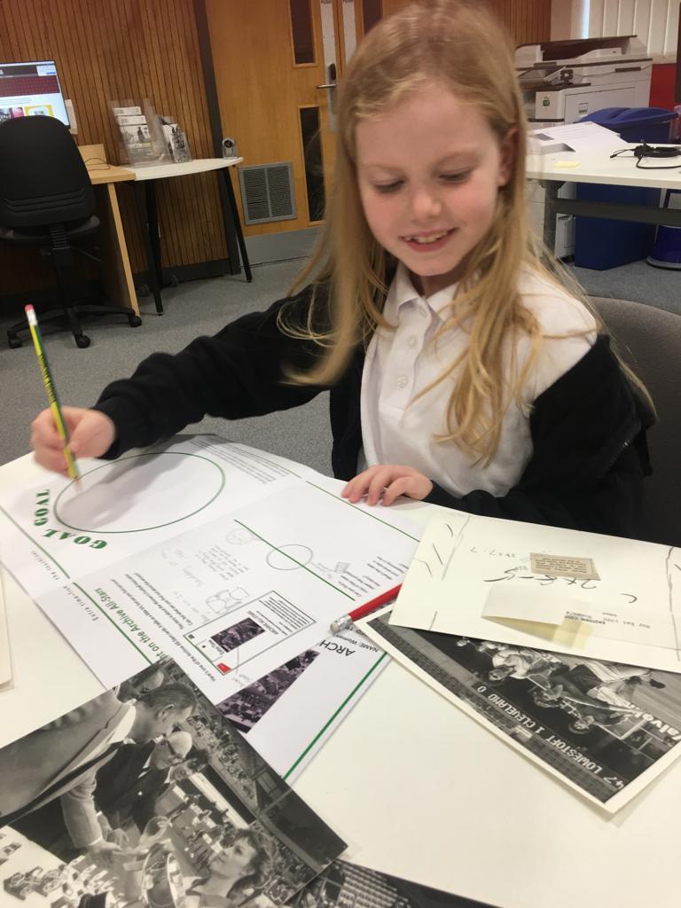 A child in white T-shirt and dark cardigan sits, pencil in hand, studying notes on the reverse of an old photograph