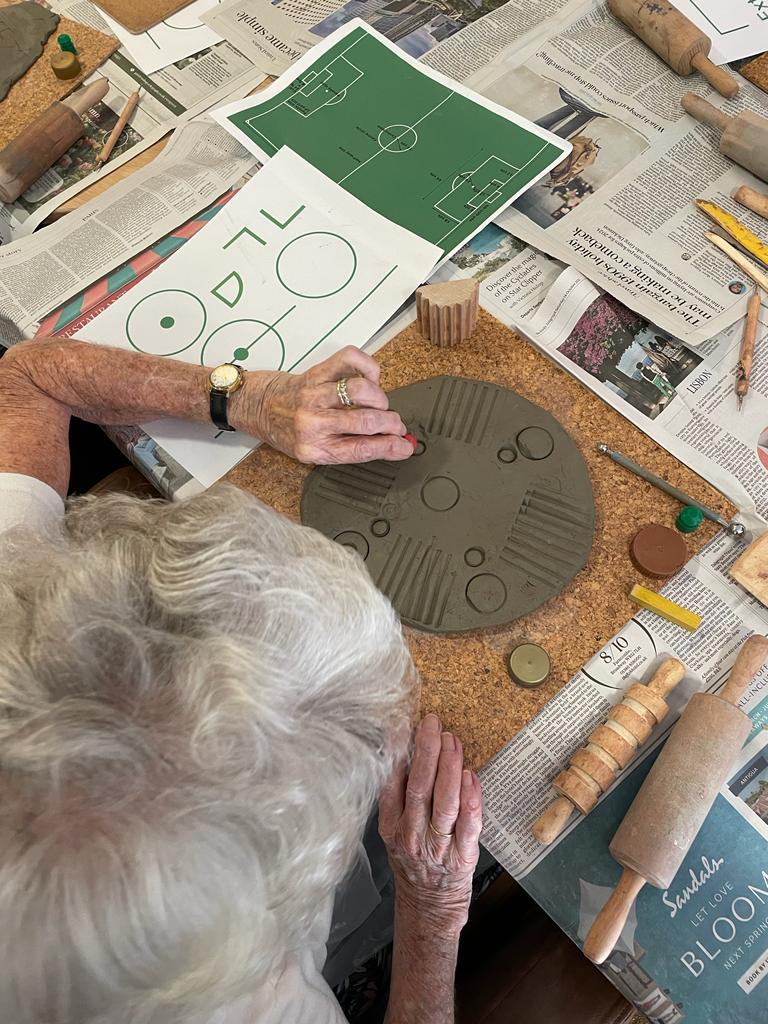 An overhead view of a lady making a series of circles and short straight lines in a clay disc