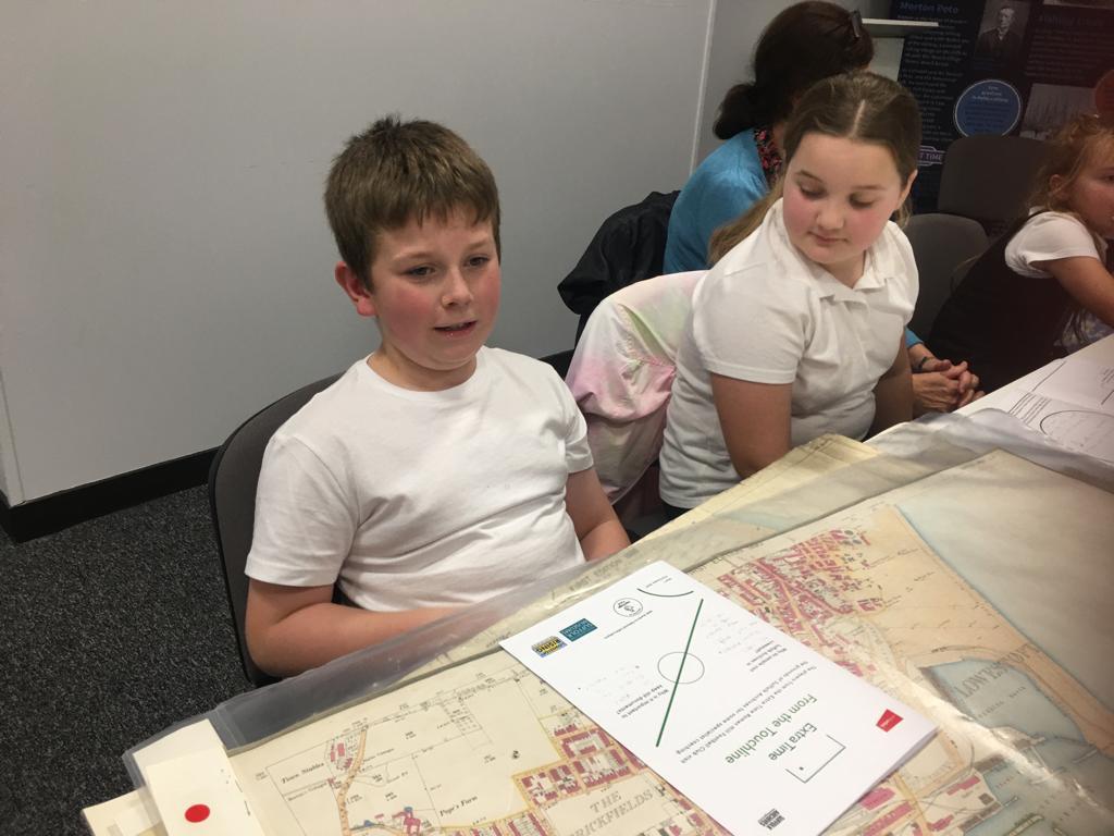 Two school children sit side by side with an old map and other documents in front of them