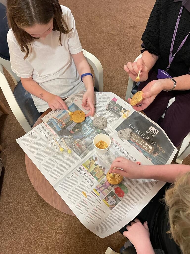 Overhead view of three people using sponge sticks to dab gold paint onto small round discs
