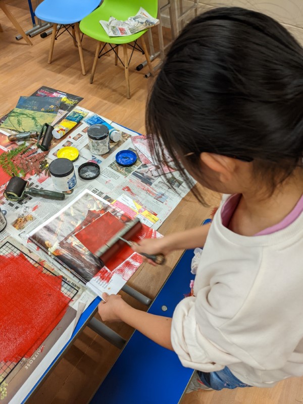 A woman is using a print roller to apply red ink/