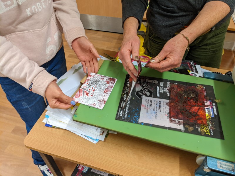 A close up photo of artist Jac Campbell and workshop participant using a printing press