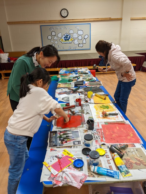 A family is creating pints together, working at a long table strewn with print rollers of different colours